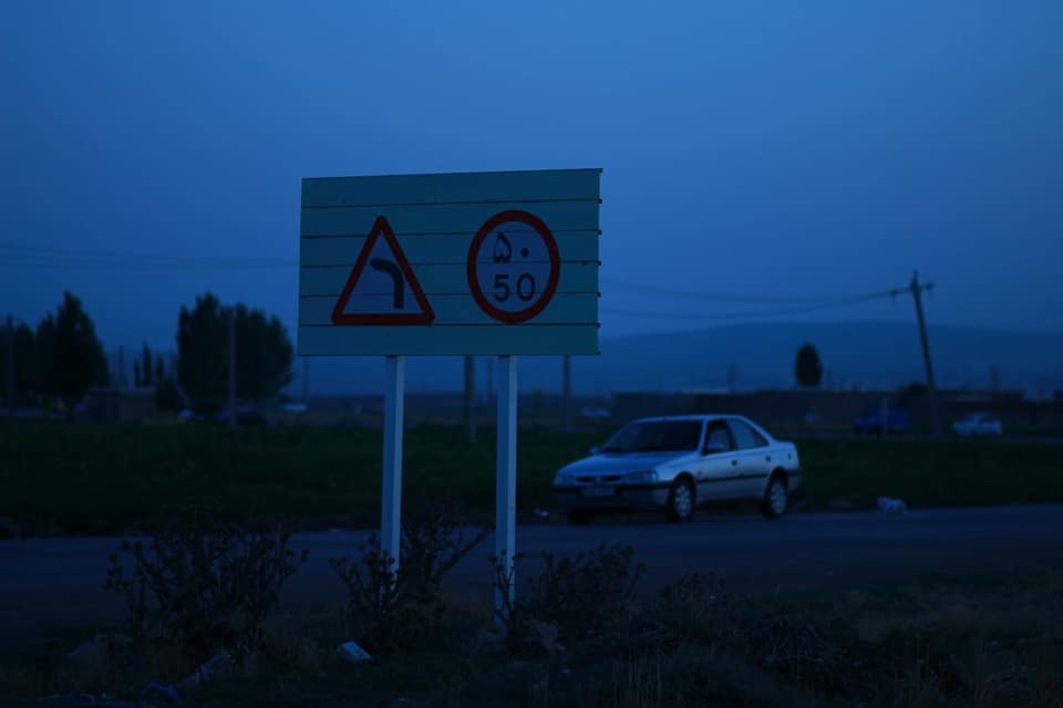 A road sign with a curve warning and speed limit beside a parked car