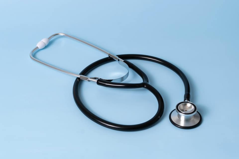 A black medical stethoscope with silver chest piece on a light blue background