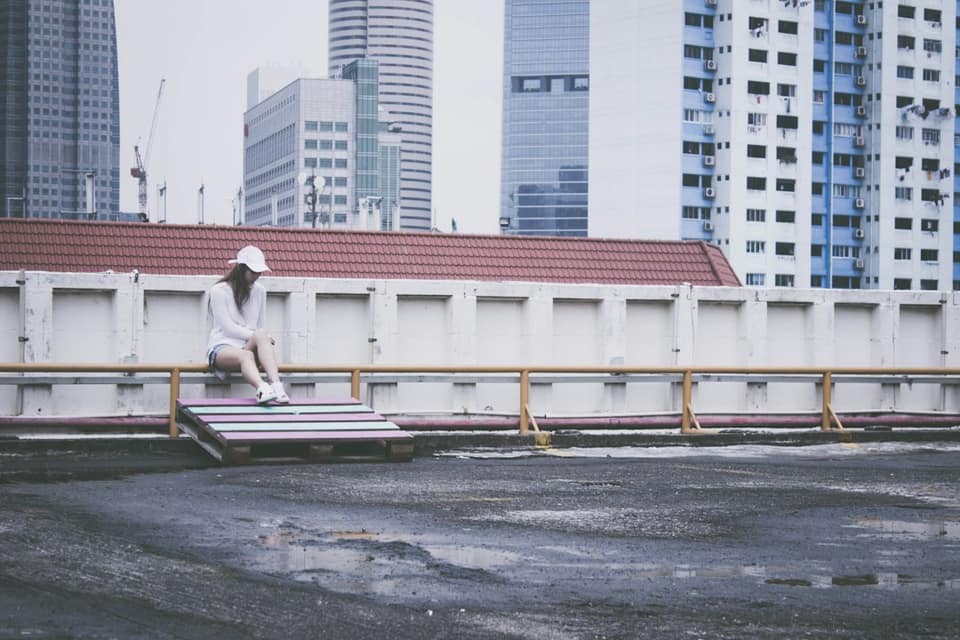 Man in white t-shirt sitting on bench near high rise buildings during daytime