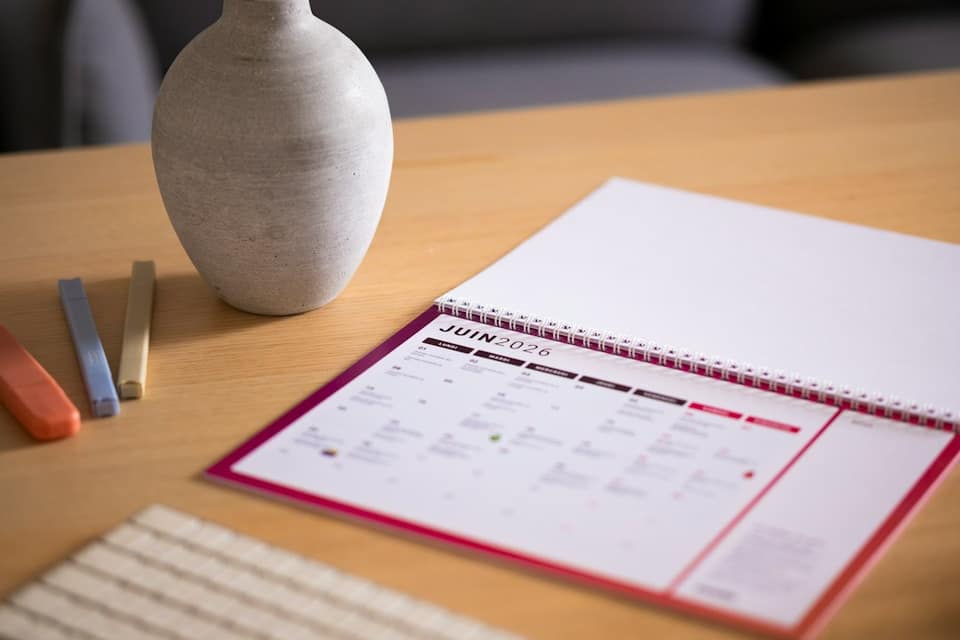 A calendar and vase sit on a wooden desk