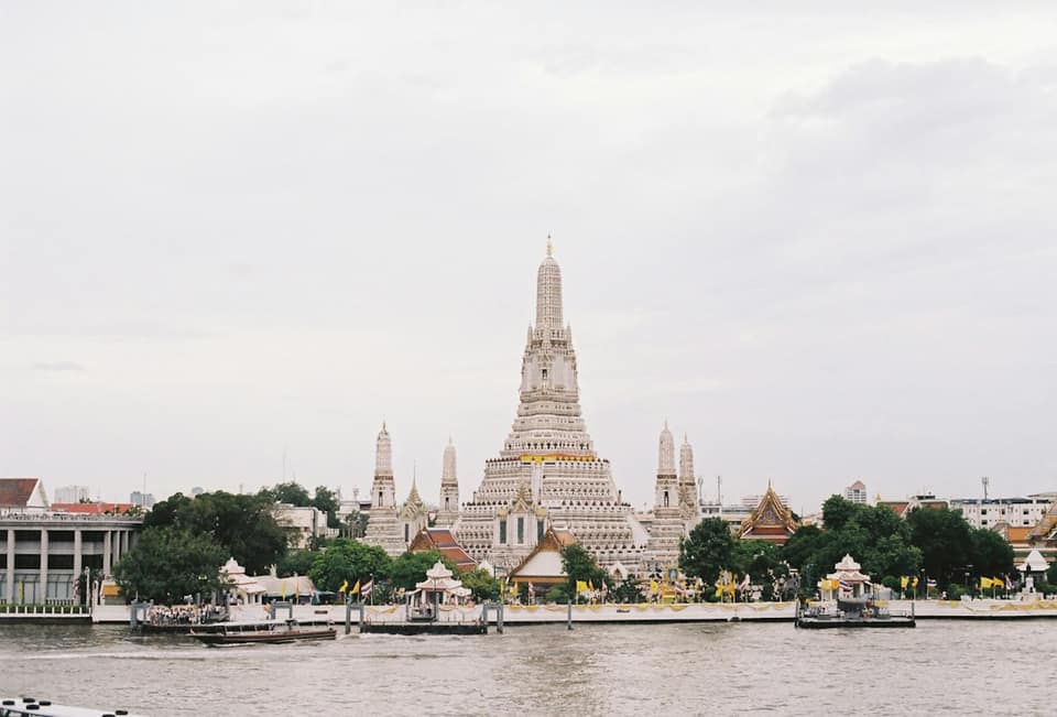 A large building with pointy towers by a body of water with Wat Arun in the background