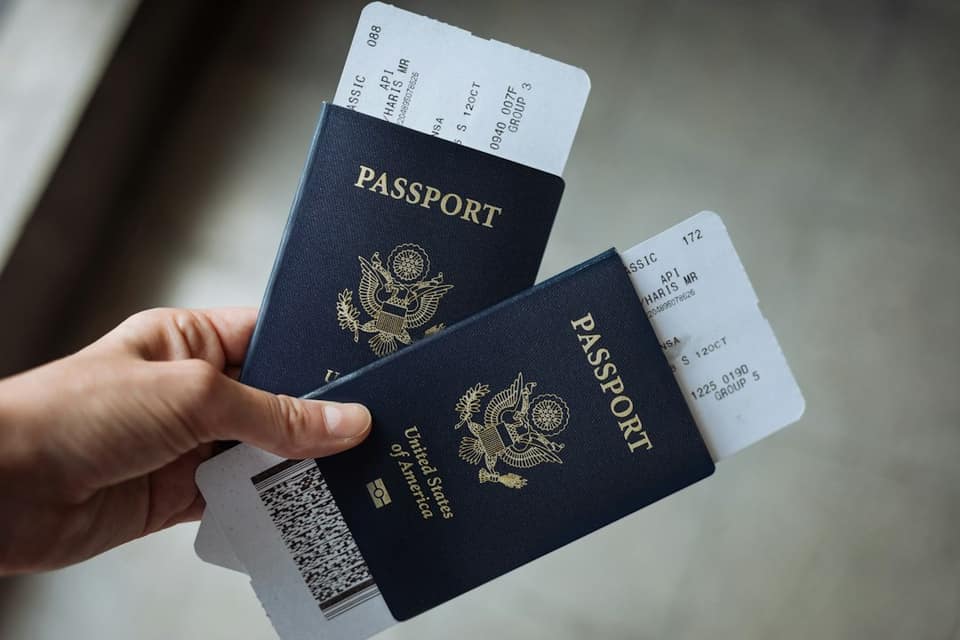 A hand holding two United States passports with airline boarding passes tucked inside